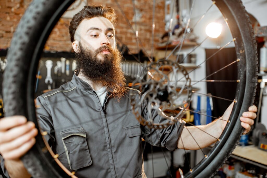 Beau réparateur barbu dans les vêtements de travail maintenant la roue du vélo avec des pauses à disque à l'atelier de vélo
