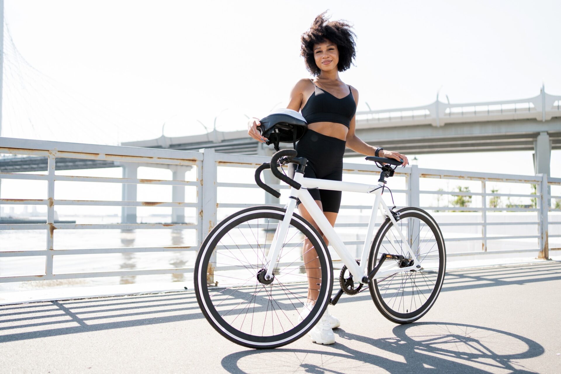 Femme sportive avec un vélo élégant sur un pont ensoleillé, prêt pour une aventure à cyclisme urbaine.